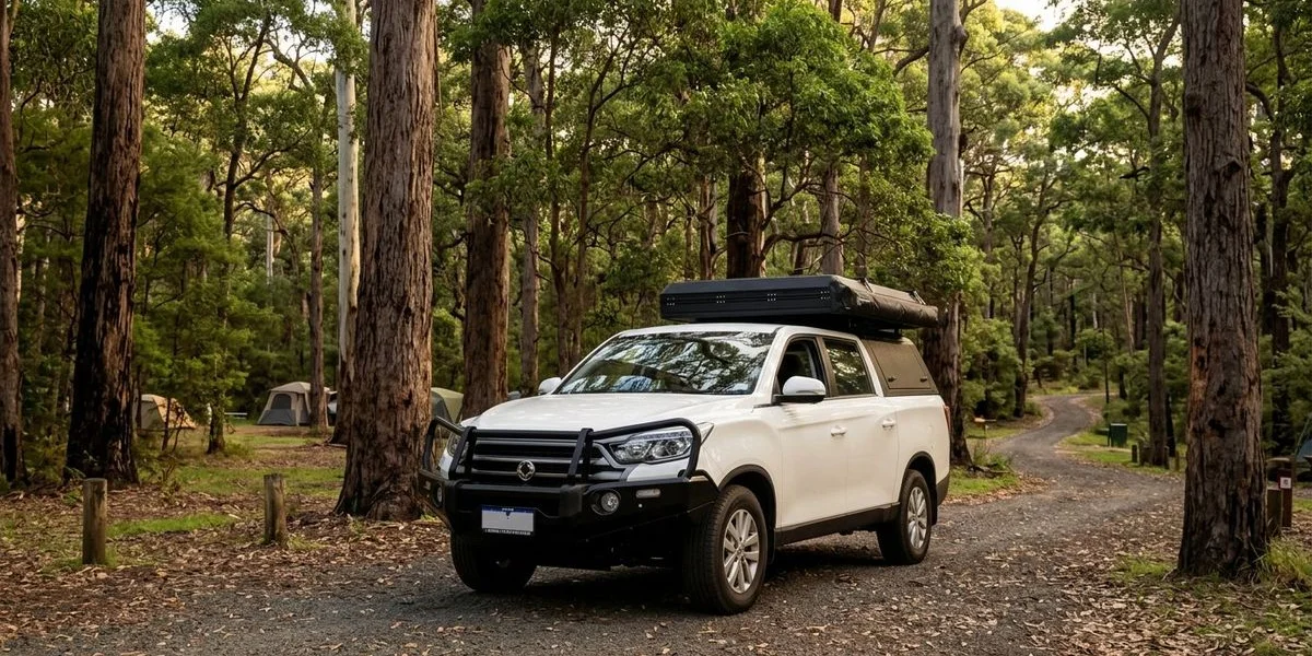 A 4WD camper parked beneath towering karri trees at a peaceful campground in the Margaret River region of Western Australia
