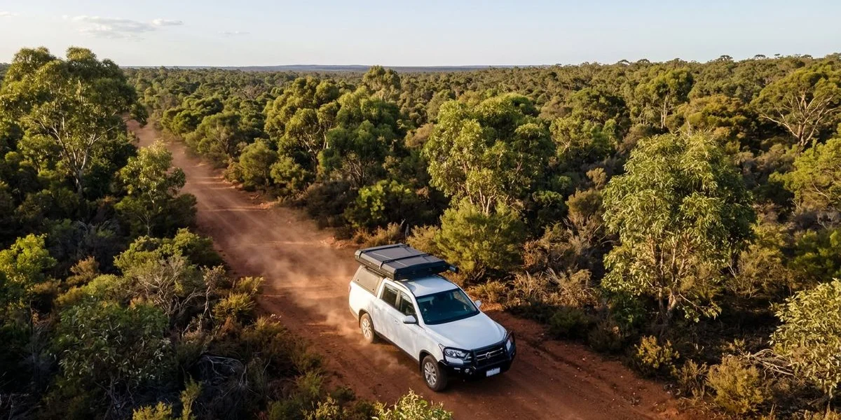 Aerial view of a 4WD camper travelling along a remote red outback road stretching through vast Western Australian bushland towards the horizon